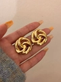 Close-up of golden knotted spiral earrings held in palm showing hollow metal details - Gold