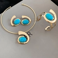 Detail of gold jewelry set featuring oval turquoise stones on a smooth grey surface - Gold Blue Set