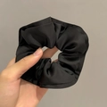 Detailopname van grote zwarte satijnen scrunchie met gelaagde plooien en subtiele glans - Zwart