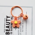 Detailed view of orange knitted flower keychain with matching bell on a white card - Orange