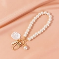 Close-up of pearl bead keychain with white shell charm and handmade metal tag on pink silk - Shell Style