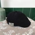 Vintage black cotton newsboy cap with side fashion label on a white lace tablecloth - Black