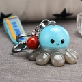 Close-up of octopus acrylic keychain with blue rubber strap and red bell detail - Blue
