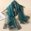 Detail of teal chiffon scarf with leopard print and chain patterns on a wooden hanger - Dark Cyan Leopard Chain