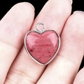 Pink natural stone heart pendant with silver metallic border held by fingers - Rhodochrosite Silver Edging