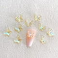 Detailed view of aurora iridescent resin butterfly charms applied on a pink nail tip - Aurora Yellow