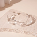 Detailed view of a transparent wavy acrylic bangle placed on a beige textured stone - White