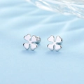 Detailed view of silver four-leaf clover stud earrings on a soft light blue fabric background - Clover - Silver