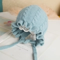 Detail of baby knit hat with ruffle edges and ties in light blue on a white stand - Light Blue - Not Lined