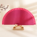 Minimalist solid wood folding fan in dark pink color displayed on a wooden stand - Rose Red