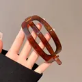 Main tenant une pince à cheveux ovale en ambre écaille avec finition résine polie - Pince Torsadée Ovale / Ambre