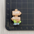 Macro shot of 3.5cm resin wooden signpost figurine with Luck and Spring text on grid mat - Luck Spring Signpost