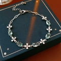 Silver bracelet with sea blue zircon stones and floral accents on a velvet jewelry box - Oval Blue Stone with Four-Petal Flower Style
