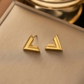 Vue détaillée des boucles d'oreilles en V dorées sur un présentoir en métal brossé - Boucles D'oreilles En V Courbé G340 En Or