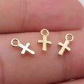 Tre piccoli ciondoli a croce dorata sulla punta di un dito mostrano la taglia 10x6mm - Oro KC