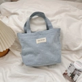 Detail of light blue denim tote bag with woven bow pattern and white brand label - Light Blue