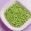 Macro detail of apple green pearlescent peanut beads in a ceramic bowl for DIY crafts - Green