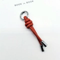 Detail view of orange knotted leather keychain with silver hardware and stitching - Tan