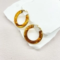 Close-up of amber resin hoop earrings with gold metal clasp on a textured white stone - Amber