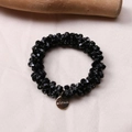 Detail of black faceted bead hair tie bracelet with a gold engraved logo tag on fabric - Black