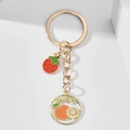 Detailed macro view of creative strawberry and orange enamel pendants on gold keychain - Strawberry Orange
