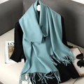 Close-up of a teal blue cashmere-feel scarf featuring soft tassels on a sofa setting - Teal