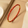 Gros plan d'un bracelet bambou doré 18K avec émail rouge vif sur un fond en soie douce - Rouge