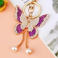 Close-up of golden butterfly keychain with purple enamel wings and pearl tassels - Purple Tassel Butterfly