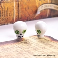 Macro view of 2cm skull charm beads with green eyes and black stitched mouth details - White Skull