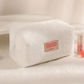 Detailed close-up of a plush white makeup bag with a pink woven patch and round zipper - White