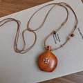 Macro detail of wooden gourd pendant with metal cross on a braided cord necklace - Coffee
