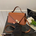 Sac à main marron en cuir gaufré avec fermoir rotatif en métal tenu dans un bureau - Brun Foncé