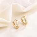 Detailopname van gouden golfvormige kleine oorringen met kralendetails op witte stof - HL-24/Gouden Gegolfde Kralenrand Creool
