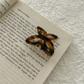 Detail of tortoise shell acetate bow hair claw clip placed on an open vintage book - Brown