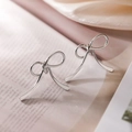 Boucles d'oreilles nœud argentées posées sur un livre ouvert avec une lumière vintage - Style Long Nœud Mince / Argenté