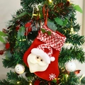 Red knitted Christmas stocking with 3D Santa Claus figure hanging on a decorated tree - Santa Claus