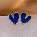 Dettaglio macro di orecchini a cuore in smalto blu con bordo dorato su seta champagne - Blu scuro