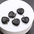 Five heart-shaped black lava stone pendants with silver metal clasps on a white podium - Lava Stone