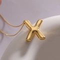 Golden balloon alphabet X pendant necklace with a polished metallic finish on white ceramic - Letter X