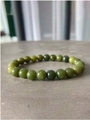 Macro view of green natural stone beaded bracelet on a textured grey stone surface - Grass Green Jade