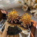 Macro detail of golden firework stud earrings with crystals on a reflective wood base - Gold