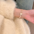 Elegante pulsera de perlas y cadena dorada con dije de camelia blanca en la muñeca - Pulsera de Perlas y Camelia