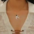 Gros plan d'un collier pendentif oiseau en or rose porté sur un col en dentelle - Collier Oiseau (avec Perle Verte A-215) / Or KC