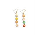 Close-up of golden drop earrings with multi-colored enamel daisy flower charms - Earrings / Colorful