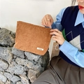 Close-up of brown corduroy cosmetic bag held by a model against a rustic stone wall - Brown