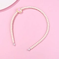 Detalle de diadema de perlas blancas con dije de corazón rosa sobre fondo rosado - Blanco