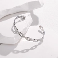 Dettaglio dell'elegante bracciale rigido a catena su un supporto in pietra bianca minimalista - Color Acciaio
