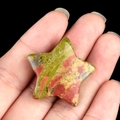 Polished unakite star stone with green and pink texture held in hand on black background - Unakite