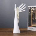 White resin hand-shaped jewelry stand holding pearl necklace and rings on wooden desk - Long Pole Hand
