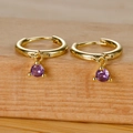 Close-up of golden hoop earrings featuring a vibrant purple round zircon drop charm - Gold Purple Zircon
